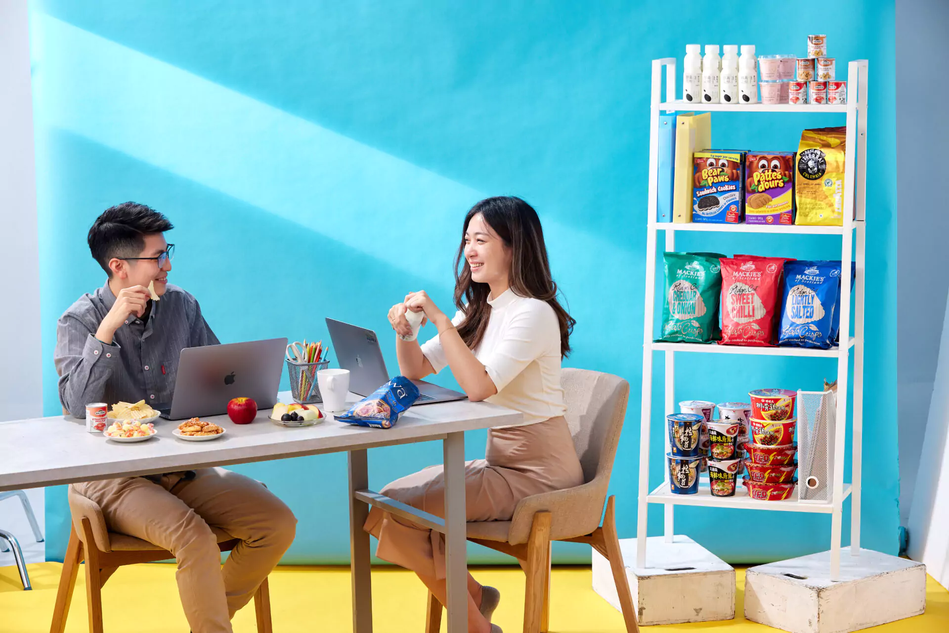 歪國零食嘴工作環境，辦公桌、人物、零食架，桌上有飲料水果點心電腦泡麵
