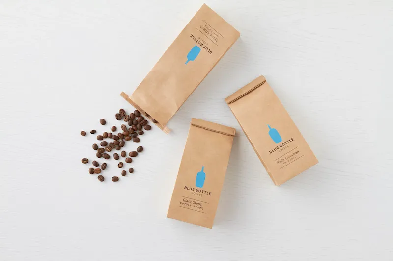 有三包藍瓶咖啡的咖啡豆，其中有一包打開散落在桌面上